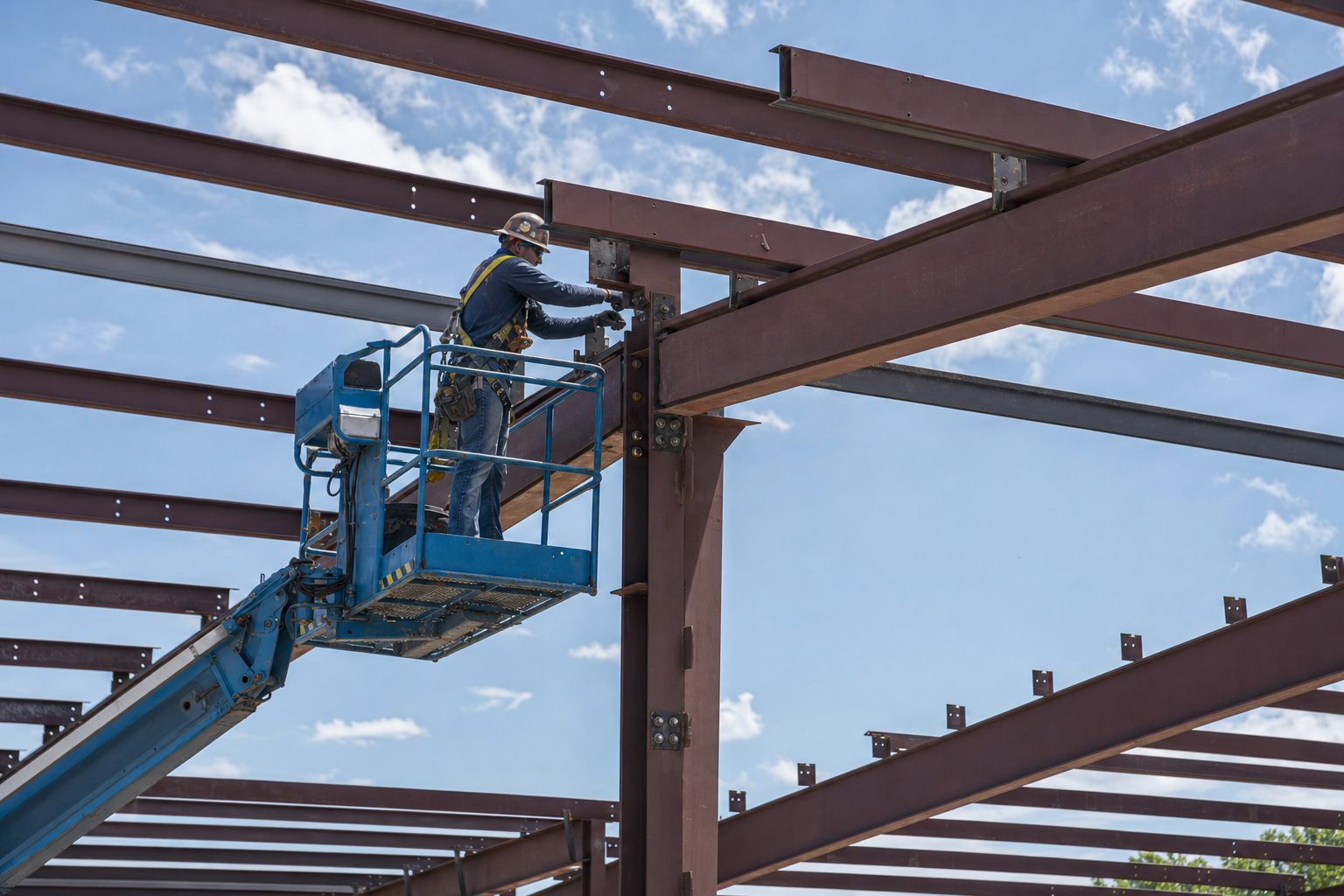 Ironworker bolting red-iron steel connections from a boom lift